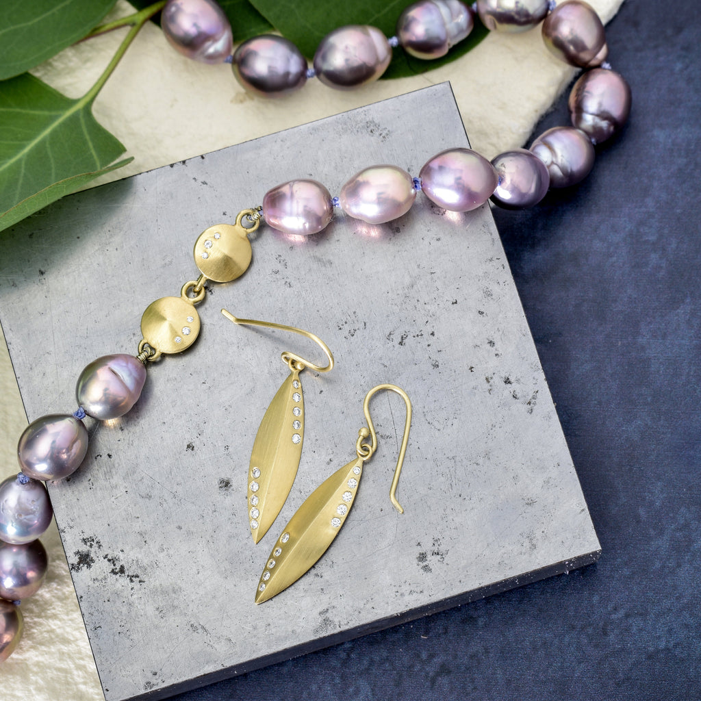 Gold earrings and necklace with purple pearls on a gray surface