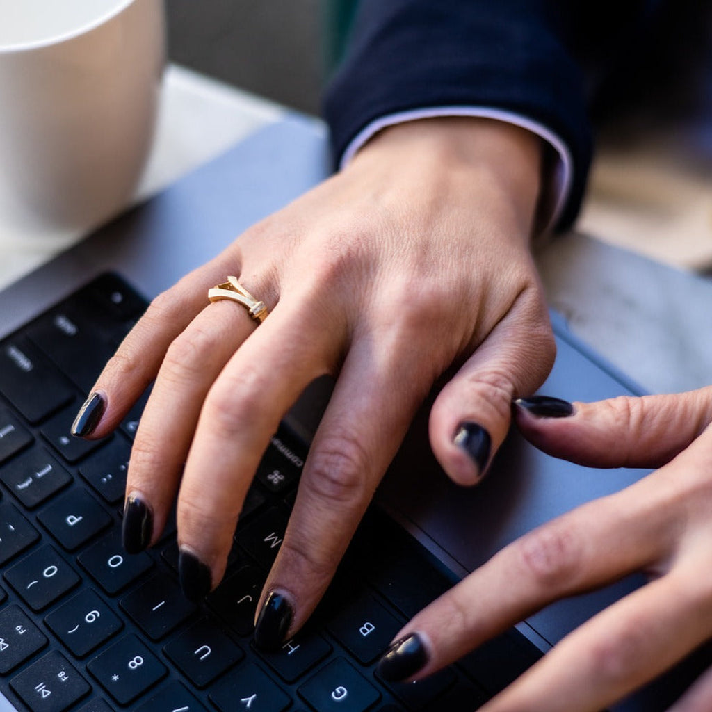 woman typing on computer wearing a trumpet shaped ring in gold with diamonds from Nikki Lorenz Designs