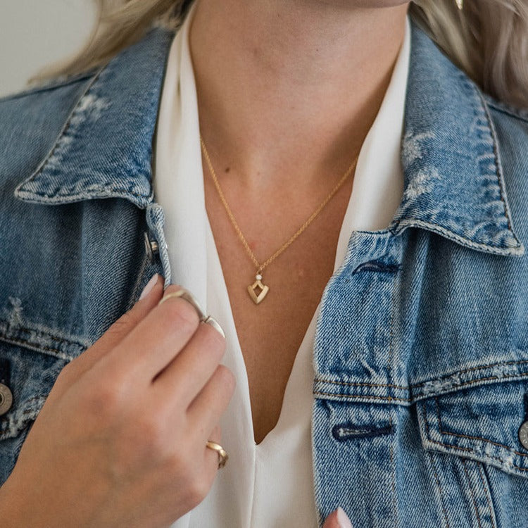 woman wearing denim jacket, white blouse, and gold and diamond small shield shaped pendant from Nikki Lorenz Designs