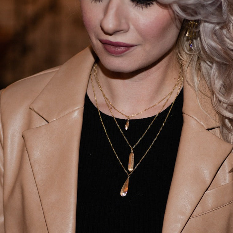 woman in tan jacket and black shirt wearing gold and diamond layering necklaces