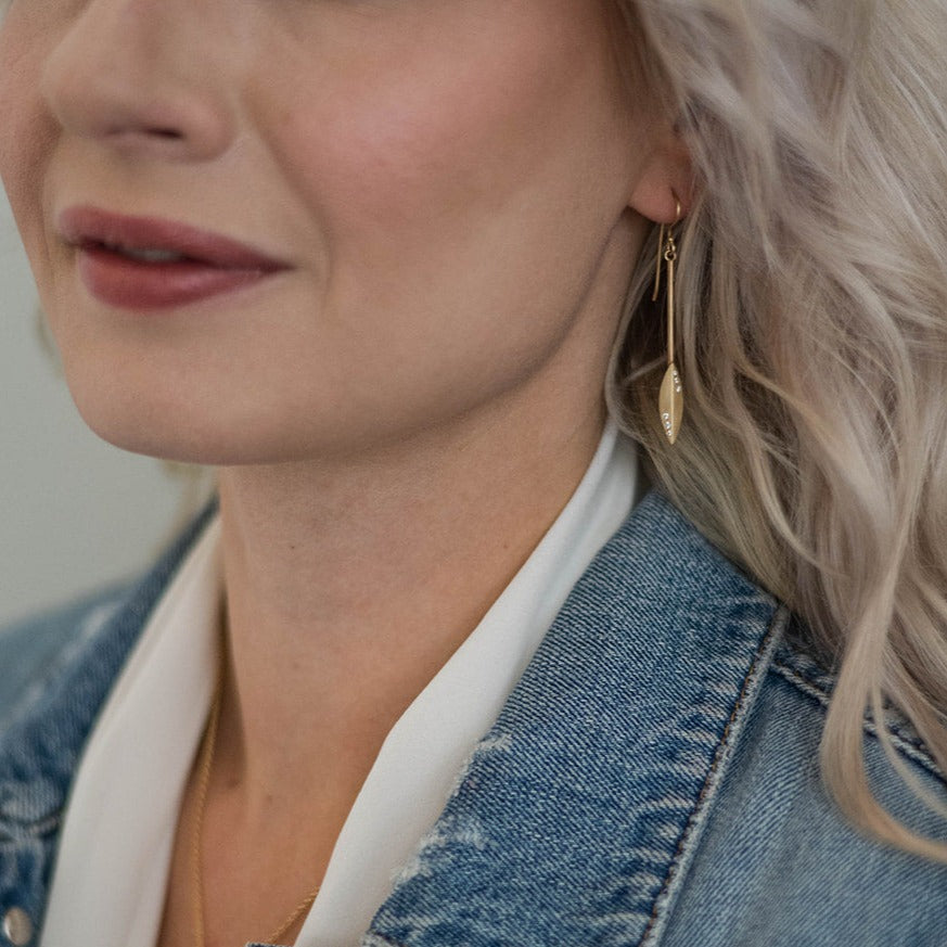 woman in denim jacket and white blouse wearing gold and diamond stiletto earrings from Nikki Lorenz Designs